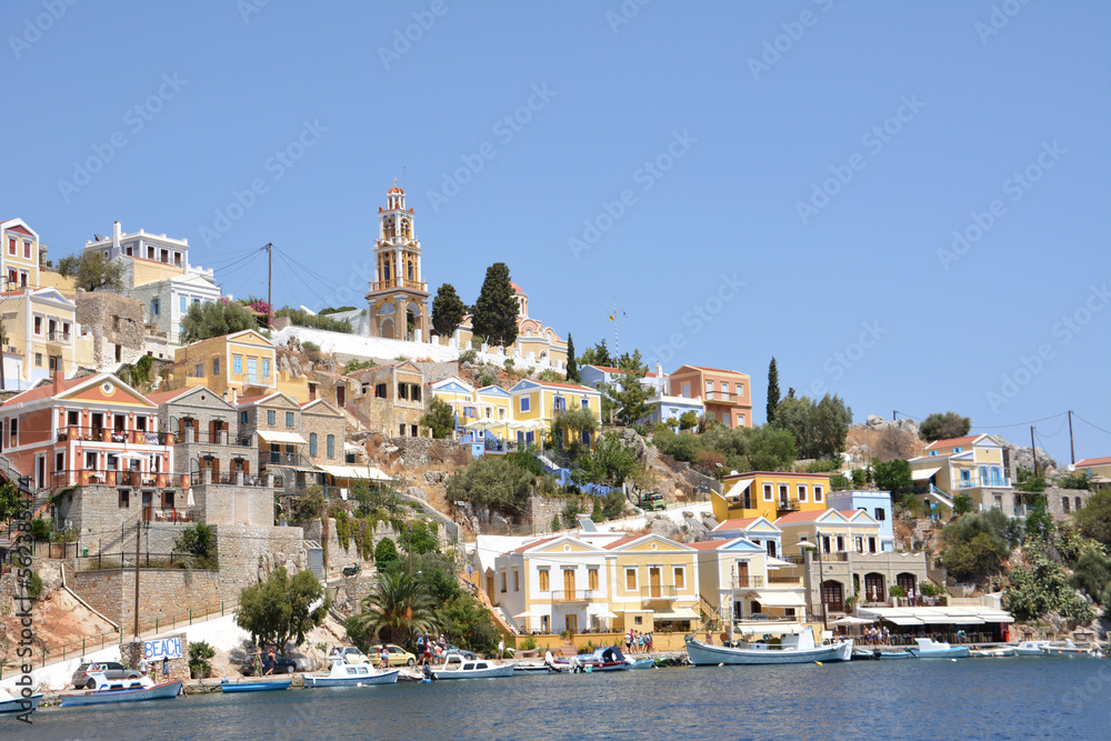waterfront with boats and painted buildings of greek island Symi with blue sky on background