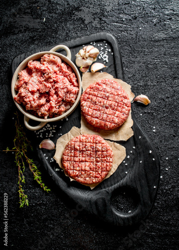 Raw burgers and ground beef on a cutting Board with garlic and thyme.
