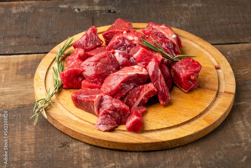Beef meat diced raw with rosemary on a round shaped cutting board and wooden background.