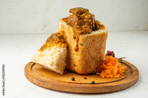 South African fast food dish bunny chow curry with meat and vegetables in white bread on a light background.