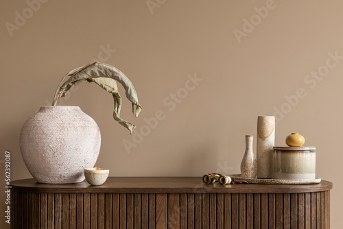 Bild auf Leinwand Interior design of living room interior with beige vase with dried leaves, beige casket, trace, wooden sideboard, brown wall and personal accessories