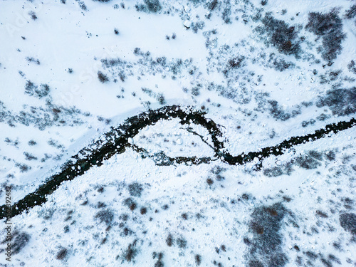 Small river stream curve aerial view during winter covered in snow.