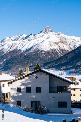 Small town with church under snow covered mountains with tres during winter in Zuoz, Switzerland.