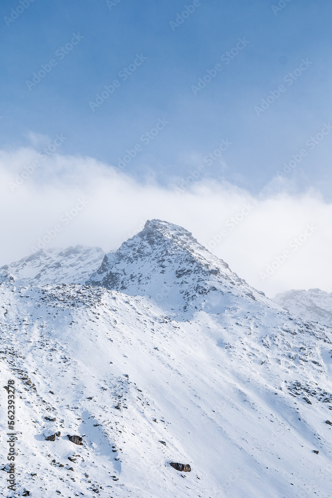 Snow covered peaks of mountains during winter on a sunny day with clouds in Fluela Pass, Davos, Switzerland.