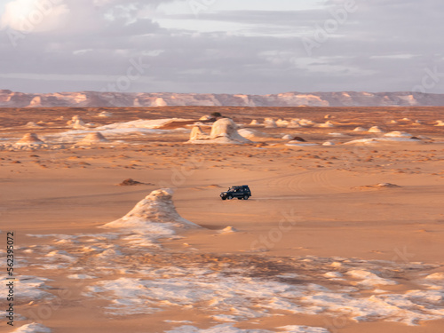 Dark jeep 4x4 driving through the landscape of White Desert, Egypt during sunset. 