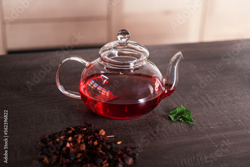 A glass teapot with red tea and fresh mint on the table.