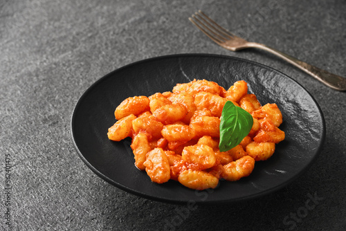 A plate of POTATO GNOCCHI in tomato sauce and a basil leaf on a stone backdrop. High angle view.