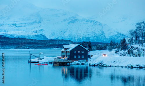 Traditional type of seasonal house in Norway on sea coast and snow covered mountain in fog at dusk - Tromso, Norway