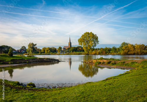 Meuse river, a natural border between dutch provinces of Gelderland and North Brabant, church of Batenburg mirrored in the river surface