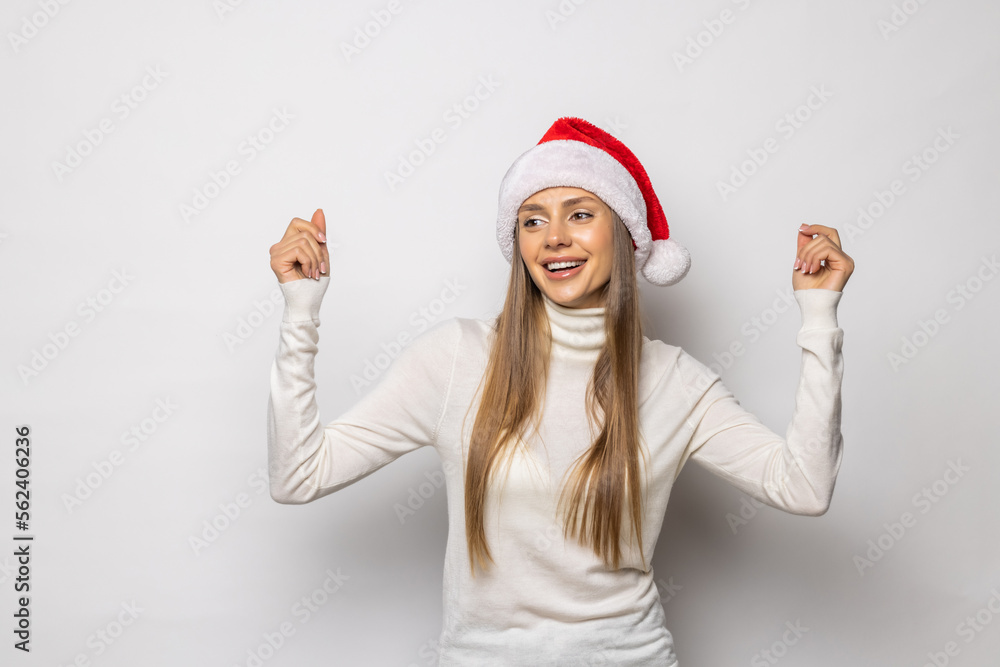 Young woman wearing a Santa hat over white background very happy and excited making winner gesture with raised arms, smiling and screaming for success. Young woman wearing a Santa hat over white background very happy and excited making winner gesture with raised arms, smiling and screaming for success.