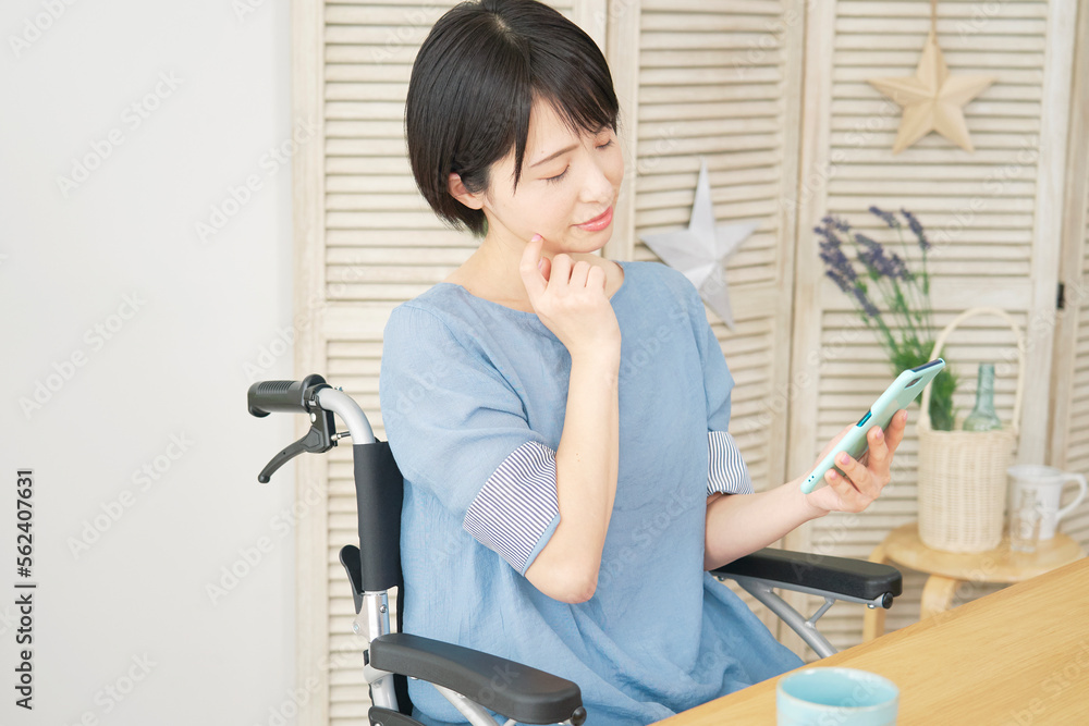 家でスマホでを持って考える車椅子に乗った障がい者女性 家でスマホでを持って考える車椅子に乗った障がい者女性