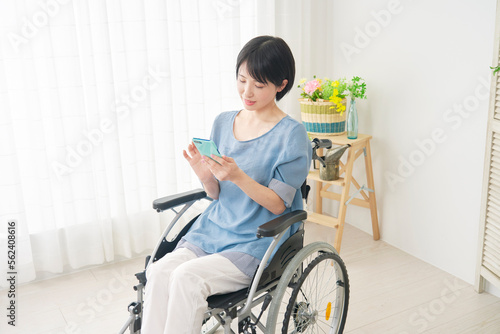 家でスマホを使う車椅子に乗った障がい者女性