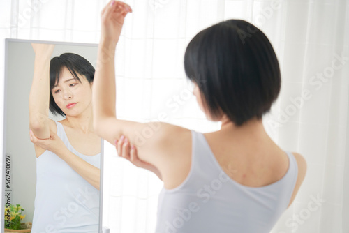 鏡の前で二の腕の贅肉を摘む女性