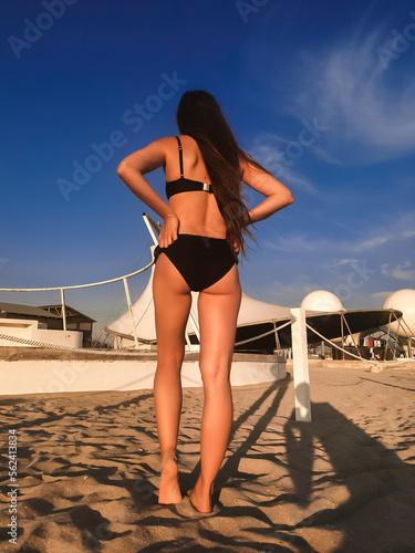 A young beautiful woman with long hair in a swimsuit dreamily looks at the beach with the sea in the background