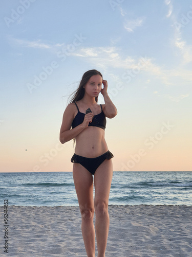 Fototapeta Naklejka Na Ścianę i Meble -   beautiful woman with long hair in a bikini dreamily looks at the beach and rests with the sea in the background