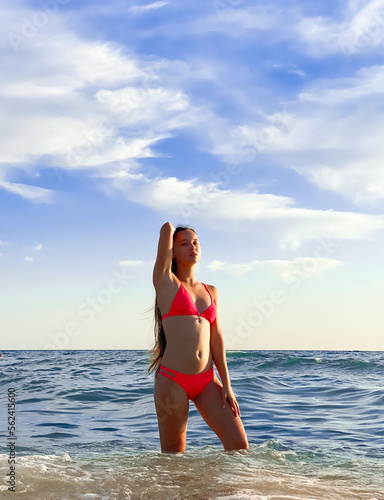 A young beautiful woman with long hair in a swimsuit dreamily looks at the beach with the sea in the background