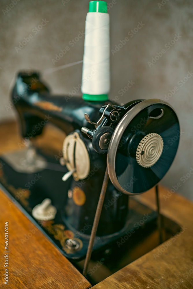 Naklejka premium Senior woman in spectacles use sewing machine. wrinkled hands of the old seamstress.elderly woman . Old sewing machine Classic retro style manual sewing machine ready for sewing work.