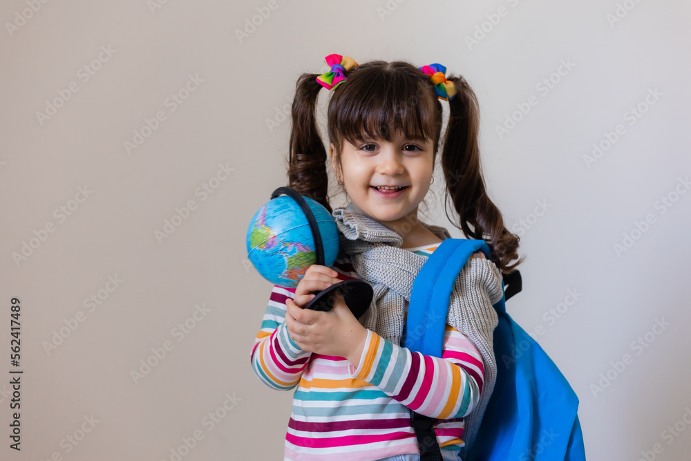 a happy little preschool girl with a backpack and a globe on a light background, space for text. Preschool education, traveling with children a happy little preschool girl with a backpack and a globe on a light background, space for text. Preschool education, traveling with children