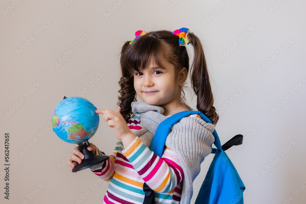a happy little preschool girl with a backpack and a globe on a light background, space for text. Preschool education, traveling with children a happy little preschool girl with a backpack and a globe on a light background, space for text. Preschool education, traveling with children