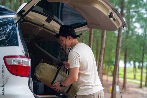 Asian man enjoy outdoor lifestyle on road trip hiking and camping on summer holiday travel vacation. Handsome guy taking off camping supplies and equipment from car trunk at natural park forest. photo