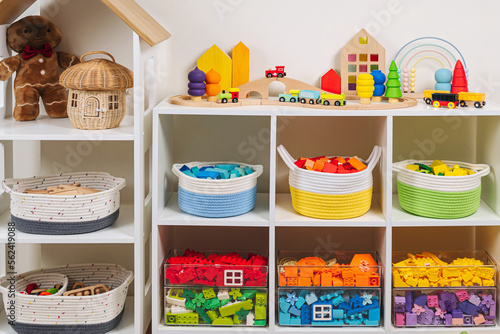 White shelving with colorful storage baskets and transparent boxes in children room. Rainbow toys in stylish baskets and plastic containers. Organizing and Storage Ideas in playroom. Interior design.