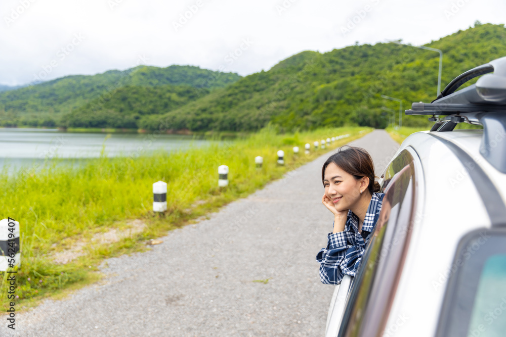 Young Asian woman enjoy outdoor lifestyle road trip and camping in forest mountain on summer travel vacation. Happy attractive girl sitting in driving car with pull her face and hand out of car window