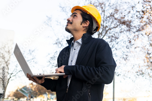 Young ethnic male engineer using netbook near modern building photo