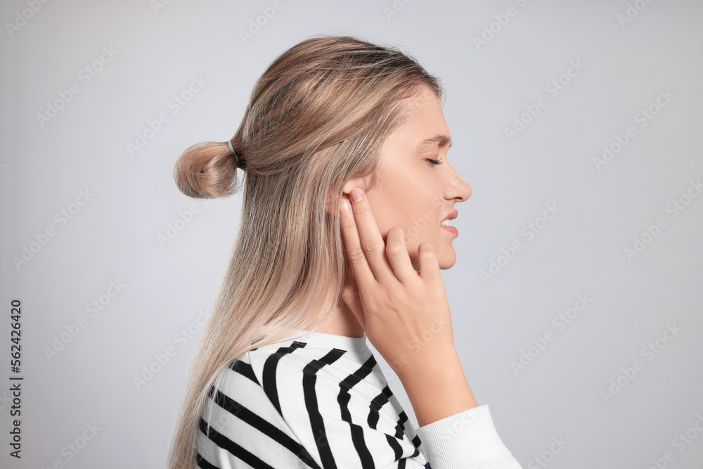 Young woman suffering from ear pain on light grey background Young woman suffering from ear pain on light grey background