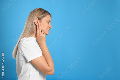 Young woman suffering from ear pain on light blue background. Space for text