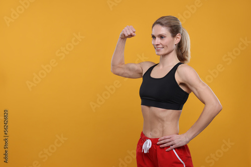 Portrait of sportswoman showing muscles on yellow background, space for text