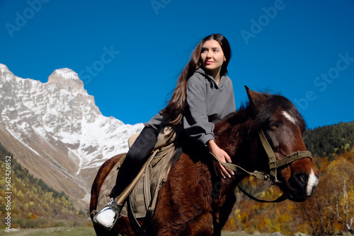 Young woman riding horse in mountains on sunny day. Beautiful pet