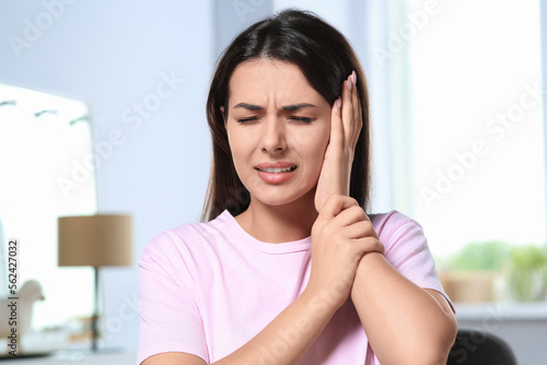Young woman suffering from ear pain indoors photo