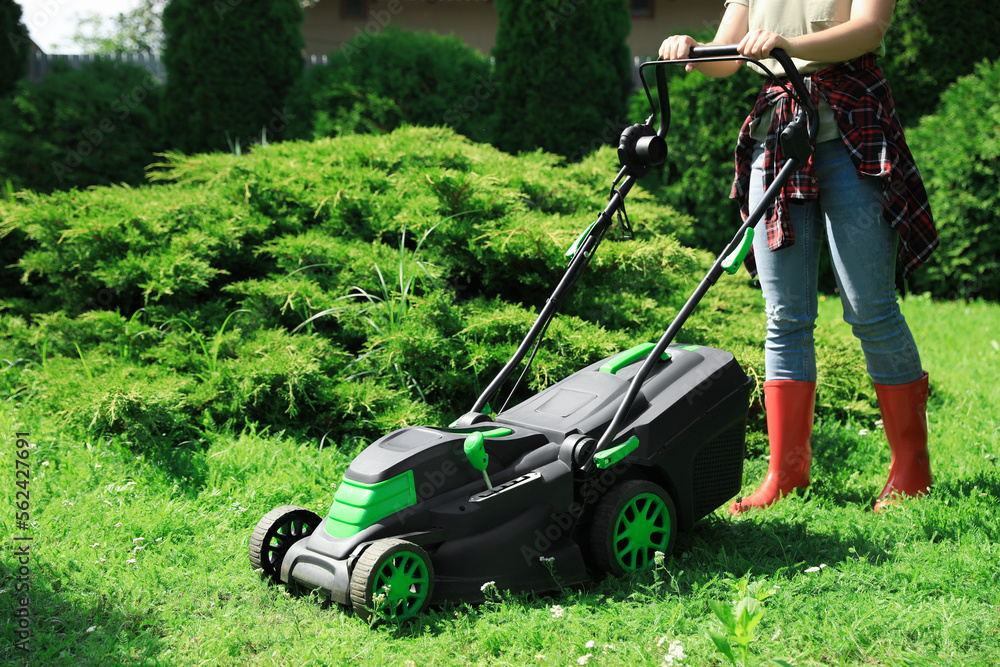Woman cutting grass with lawn mower in garden on sunny day, closeup Woman cutting grass with lawn mower in garden on sunny day, closeup