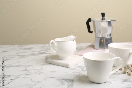 Cups, moka pot and jug on white marble table. Space for text