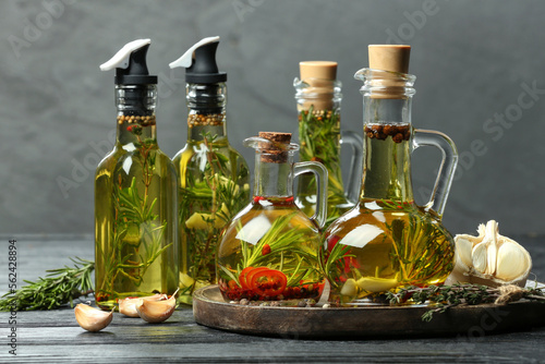 Cooking oil with different spices and herbs in bottles on grey wooden table