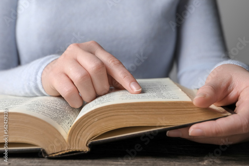 Woman reading Bible at wooden table, closeup