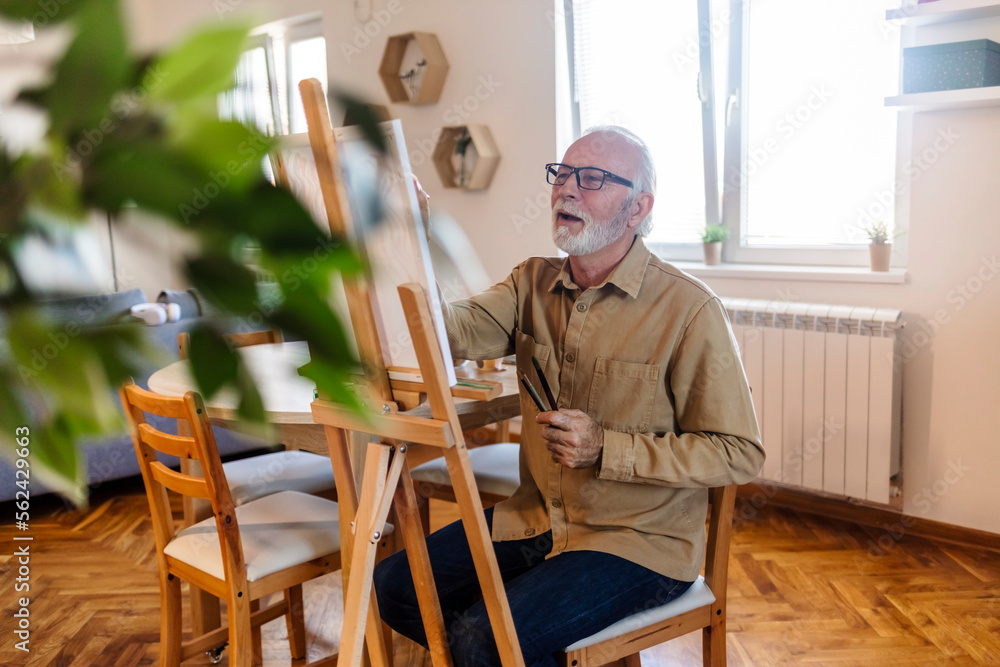 Happy retired senior man painting on canvas for fun at home