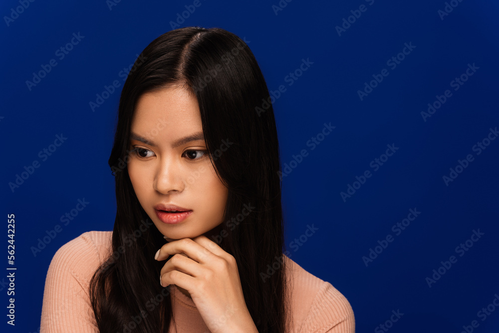 Pensive brunette asian woman looking away isolated on blue Pensive brunette asian woman looking away isolated on blue