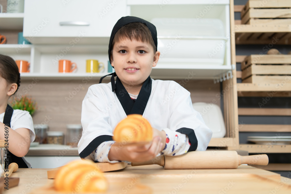 Fototapeta premium Portrait of a little boy in the kitchen of a house having fun playing baking bread