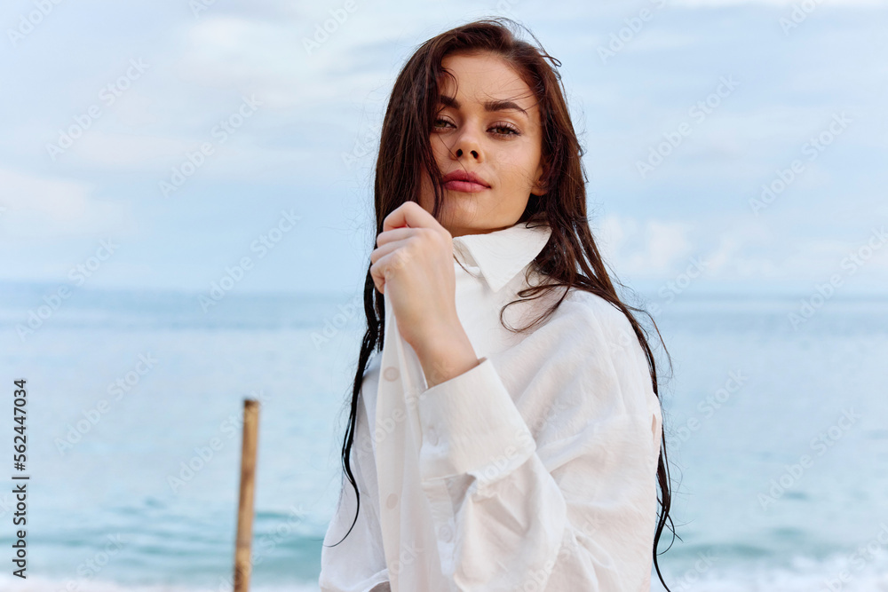 Portrait of a beautiful pensive woman with tanned skin in a white beach shirt with wet hair after swimming on the ocean beach sunset light with clouds, the concept of freedom and mental health Portrait of a beautiful pensive woman with tanned skin in a white beach shirt with wet hair after swimming on the ocean beach sunset light with clouds, the concept of freedom and mental health