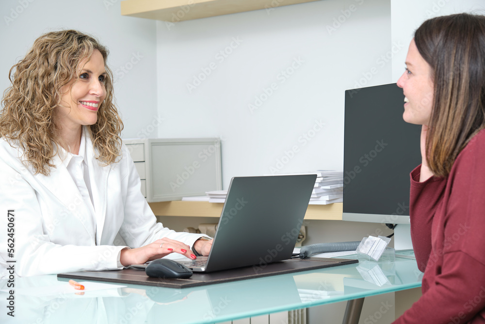 blonde female doctor and a young female patient sitting at a table in an office smiling blonde female doctor and a young female patient sitting at a table in an office smiling