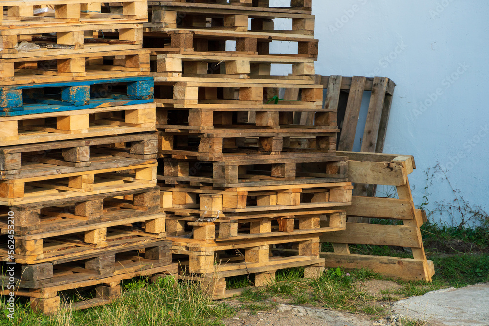 A stack of wooden pallets in an internal warehouse. An outdoor pallet storage area under the roof next to the store. Piles of Euro-type cargo pallets at a waste recycling facility.