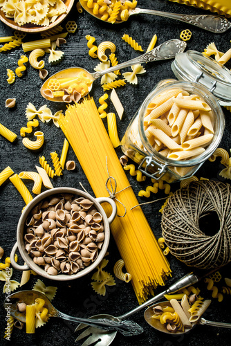 Pasta background. Assortment of different types of dry pasta in bowl and spoons with twine.