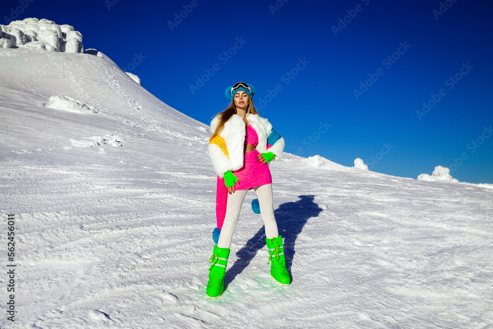 Beautiful sexy woman is wearing white fur, winter hat, scarf and winter boots. Attractive young girl in mountains.