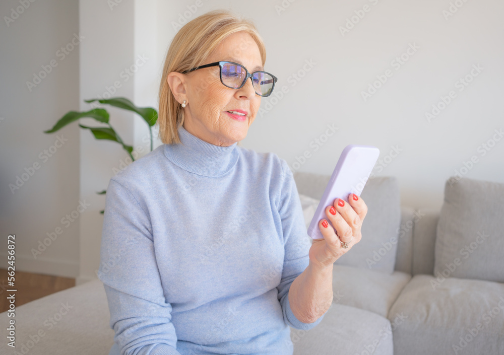 Relaxed mature old 60s woman, older middle aged female customer holding smartphone using mobile app, texting message, sitting on couch at home. Relaxed mature old 60s woman, older middle aged female customer holding smartphone using mobile app, texting message, sitting on couch at home.