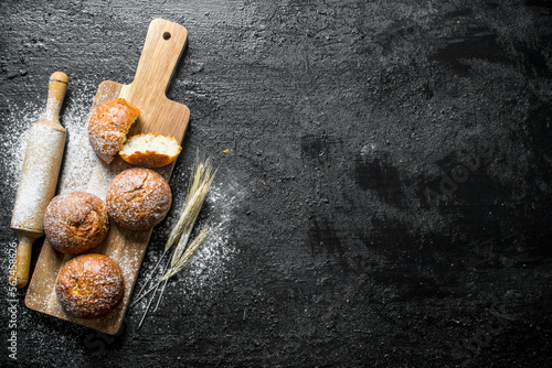 Fresh buns on a wooden cutting Board with a rolling pin and spikelets.