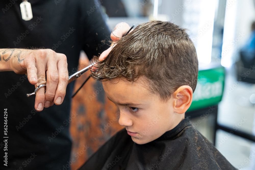 Close up view of a hairdresser cutting boy hair with scissors at barbershop. Hairdressing and childhood concept.