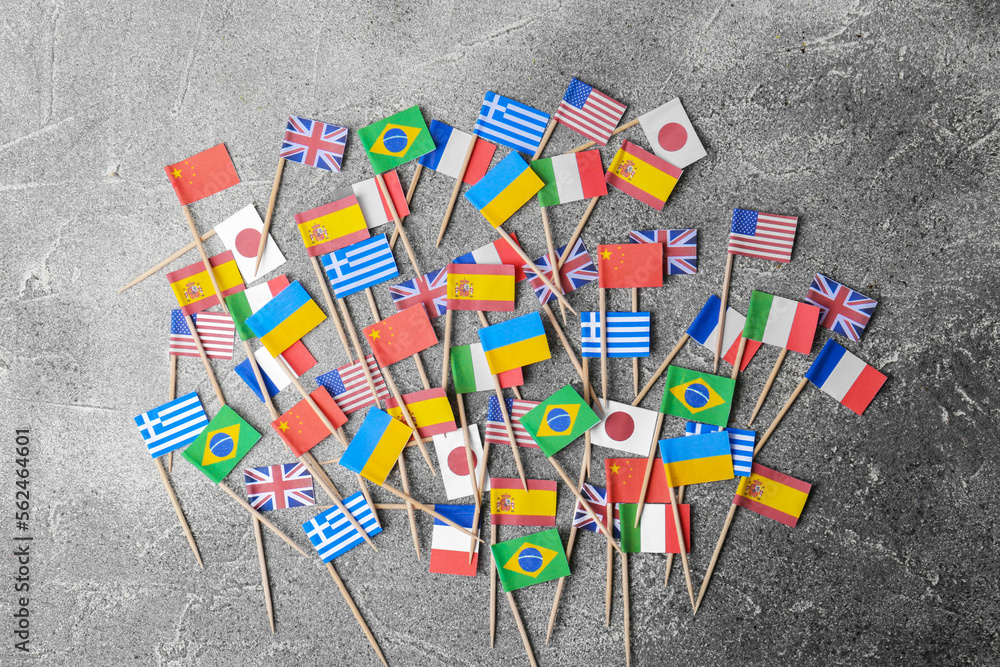 Many small paper flags of different countries on grey table, flat lay - obrazy, fototapety, plakaty 