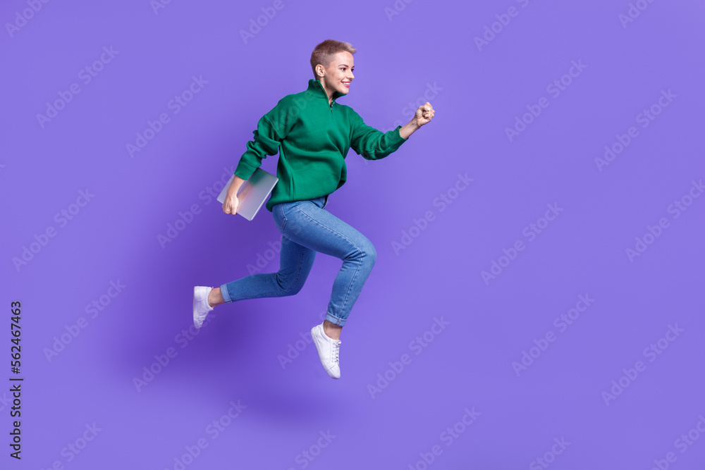 Full length photo of shiny cute woman dressed green pullover jumping running holding device empty space isolated purple color background