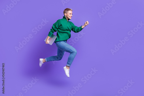 Full length photo of shiny cute woman dressed green pullover jumping running holding device empty space isolated purple color background © deagreez